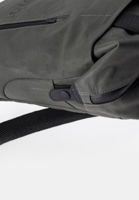 Zaino impermeabile grigio con finitura testurizzata, dettagli neri e tasca con zip, dotato di una robusta tracolla regolabile.