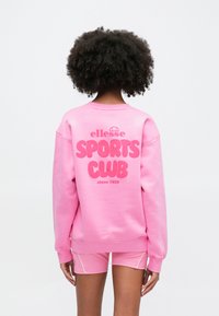 Ružová mikina s veľkým grafickým nápisom "SPORTS CLUB" na chrbte, vyrobená z mäkkej tkaniny s rebrovanými manžetami a okrúhlym výstrihom.