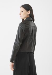 Černá ko�žená bunda s límcem, přiléhavý design, prošívané detaily a patentky. Nositá přes černou plisovanou sukni.