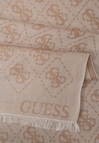 Bežna šal s vzorcem logotipov S in C, z resastim robom in izpisom besede "GUESS" v tkanju. Mehka tekstura in diagonalni šivi.