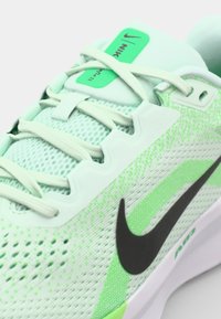 Lys grøn atletisk sko med mesh-overdel, sort Swoosh-logo, teksturerede detaljer og hvid sål. Har flade snørebånd og polstret krave.