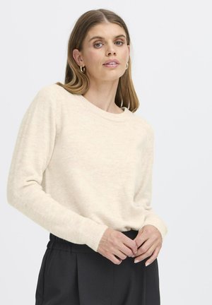 Beige hosszúujjú pulóver kerek nyakkivágással és bordás mandzsettával, puha, texturált anyagból készült. Sötét, laza nadrággal párosítva.