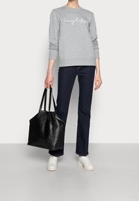 Grijze sweatshirt met wit logo, donkerblauwe jeans en een grote zwarte leren handtas, aangevuld met witte sneakers. Eenvoudig en modern ontwerp.