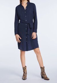 Granatowa sukienka koszulowa z zapięciem na guziki, przewiązana w talii, z długimi rękawami i pionowym prążkowanym wzorem, w połączeniu z botkami w wężowy wzór do kostek.