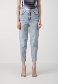 Kvinna som bär ljusblå höga jeans och silverfärgade klackar med ankelremmar, tillsammans med en svart- och vitrandig ärmlös topp.