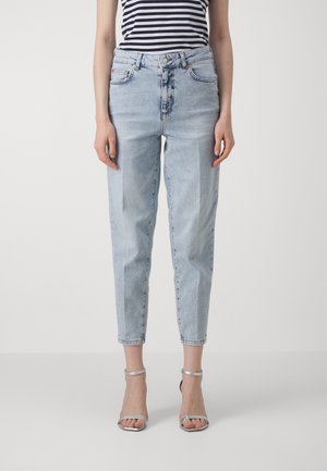 Mujer vistiendo jeans de tiro alto en azul claro y tacones plateados con cinta en el tobillo, combinados con una blusa sin mangas a rayas en blanco y negro.