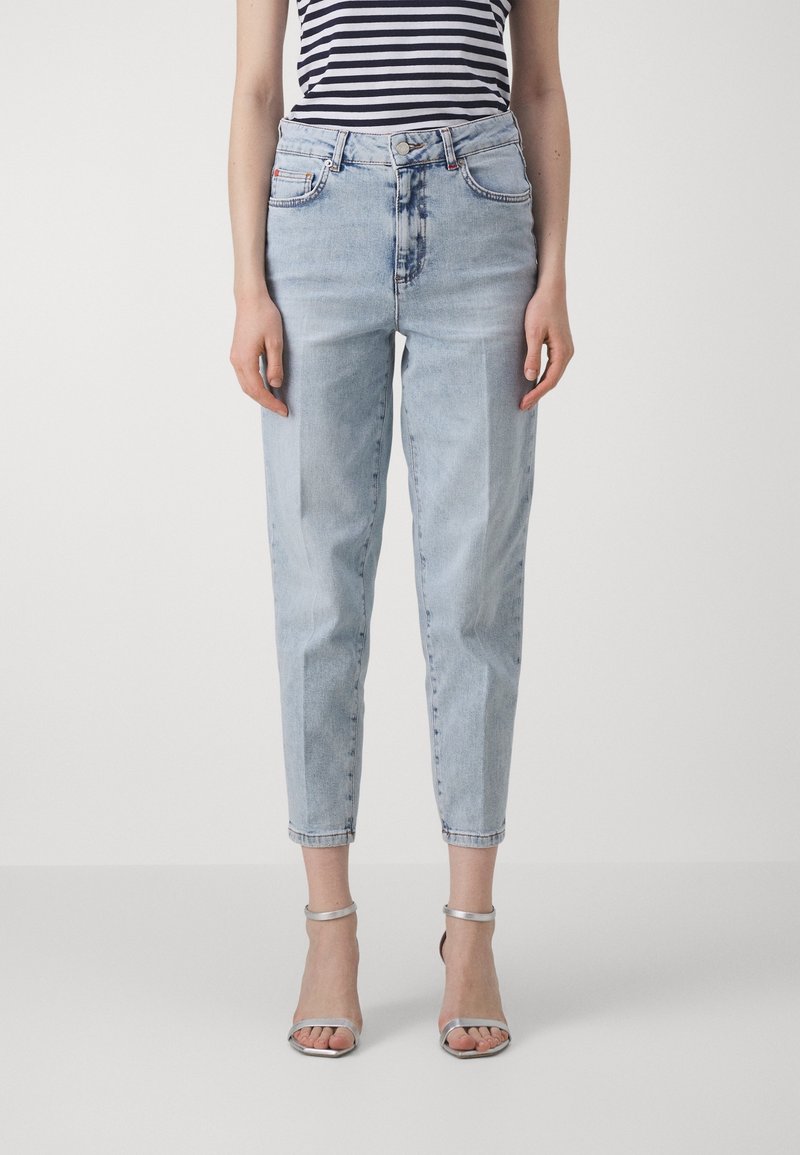 Kvinna som bär ljusblå höga jeans och silverfärgade klackar med ankelremmar, tillsammans med en svart- och vitrandig ärmlös topp.