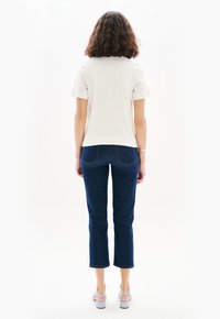 Vit kortärmad t-shirt kombinerad med mörkblå croppade jeans. Jeansen har stickade bakfickor och en figurnära design. Ljusgrå sandaler fulländar outfiten.