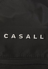 Crna tkanina s mat teksturom s imenom branda "CASALL" ispisanim u podebljanim bijelim slovima. Dizajn je elegantan i minimalističan.