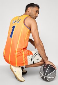 Oranžový basketbalový dres s vertikálnymi pruhmi, modrými akcentmi a menom "BALL" na chrbte. Hráč má na sebe vzorované šortky a tenisky.