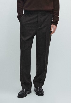 Pantaloni grigi scuri a righe sottili con una vestibilità dritta, dotati di vita con passanti per cintura e tasche laterali, abbinati a scarpe nere.