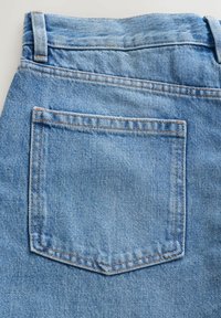 Dos d'un jean en denim bleu clair montrant une seule poche carrée avec des surpiqûres orange et des passants de ceinture sur un fond blanc.