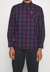 Koszula w kratę w kolorze granatowym, czerwonym i białym, z kołnierzykiem zapinanym na guziki, długimi rękawami oraz kieszenią na piersi z logo. Wykonana z bawełny.