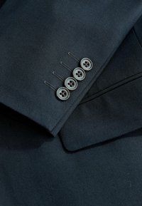 Manche de costume bleu marine foncé avec quatre boutons noirs alignés près du poignet et détails visibles du tissu texturé.
