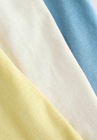 Trois échantillons de tissu qui se chevauchent : jaune pâle, crème et bleu clair. Les matériaux sont doux, avec une texture lisse et un léger éclat.