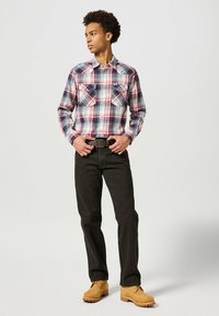 Chemise à manches longues à carreaux rouge, bleu et blanc avec deux poches poitrine, associée à un jean noir et des bottes beiges à lacets.