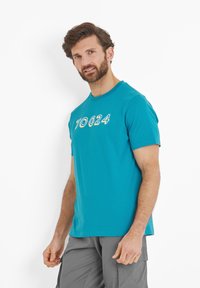 Teal cotton t-shirt with short sleeves, featuring a front logo "TOG24" in a contrasting color. Smooth texture, round neckline.