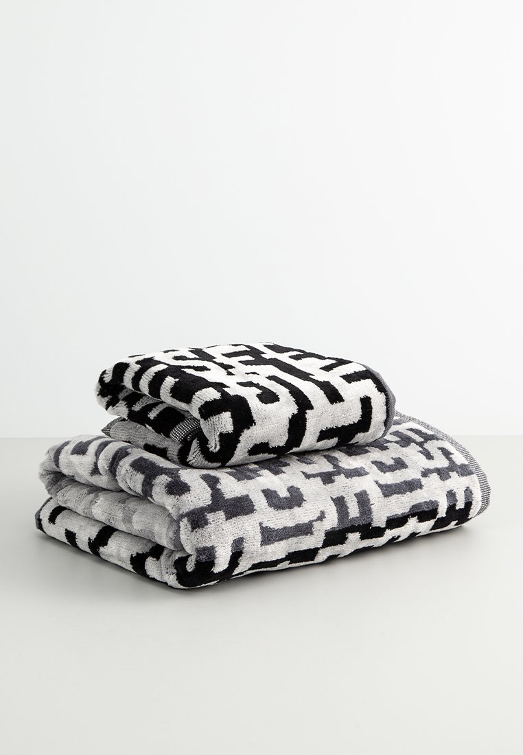 Deux serviettes pliées, l'une noire avec un motif géométrique blanc et l'autre grise avec un design similaire, mettant en valeur une texture douce et des couleurs contrastées.