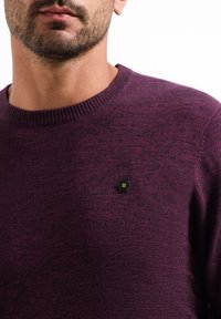 Ronde hals sweater van donkerpaars gebreid stof, met een zwart hexagonaal logo patch op de borst en een geribbelde halslijn voor extra textuur.