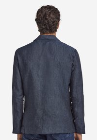 Ciemnoniebieska lniana marynarka, jednorzędowa konstrukcja, teksturowane wykończenie, klapy z wycięciem i dopasowany krój, pokazana od tyłu.