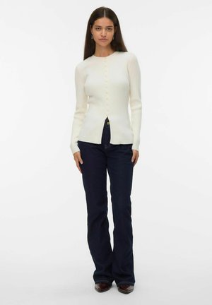 Witte geribbelde cardigan met ronde halslijn en knoopsluiting. Gecombineerd met donkere flare jeans, die een gladde textuur en een slim fit tonen.
