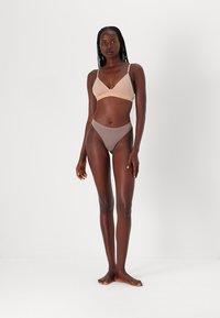 Bralette beige avec de fines bretelles, assortie à des culottes taille haute marron clair. Texture lisse, design minimaliste et sans motifs visibles.