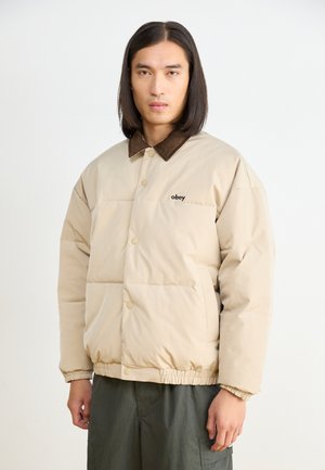 Beige gepolsterte Jacke mit einem braunen Cordkragen, Druckknöpfen, elastischem Saum und subtilen Logodetails auf der Brust.