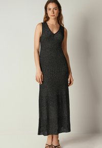 Svart, ärmlös maxiklänning med V-ringning, som har en ribbad textur och subtil glans. Vidgar sig mjukt från knäet.