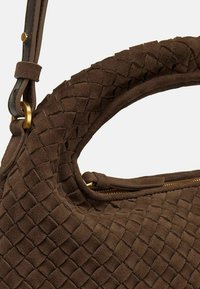 Borsa in suede marrone con texture intrecciata, manico curvo, tracolla regolabile e chiusura con zip con dettagli in hardware color oro.