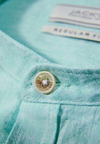 Camicia turchese chiaro con tessuto testurizzato. Presenta un bottone trasparente con un dettaglio di design e un'etichetta che legge "Taglio Regolare".