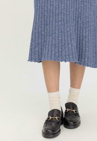 Hellblauer gerippter Strickrock mit gewelltem Saum, kombiniert mit schwarzen Lederloafers mit goldfarbenen Beschlägen und crèmefarbenen Socken.