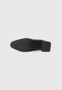 Chaussure en cuir marron avec un large talon carré, semelle texturée et finition lisse. Présente un détail de couture discret sur le côté.
