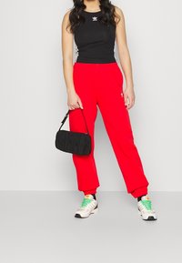 Černý crop top s bílými pruhy, červené tepláky, černá texturovaná kabelka a bílé tenisky se zelenými tkaničkami a důrazy.