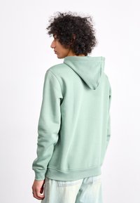 Mintgroene hoodie met een trekkoord in de capuchon, ribgebreide mouwen en onderkant. Zachte stof met een relaxte pasvorm, gecombineerd met lichtgekleurde jeans.