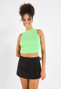 Top scurt, cu un guler înalt, de culoare verde deschis și cu striații, asortat cu o fustă mini neagră, care are un buzunar frontal și o textură netedă.