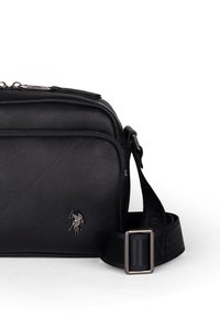Borsa a tracolla in pelle nera con logo argentato, chiusura con zip e tracolla in tessuto regolabile con motivo impresso. Texture liscia, forma compatta.