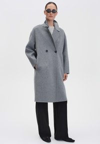 Grijze wolmix overjas met een dubbele rij knopen, grote kraag en zwarte knopen, gecombineerd met zwarte brede broek.