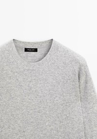 Szary sweter dzianinowy z okrągłym dekoltem, wykonany z miękkiego materiału. Tekstura jest nieco zróżnicowana, z delikatnym melanżowym wzorem.