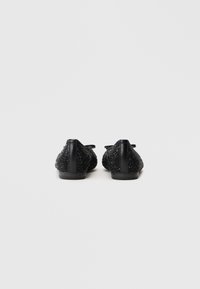 Μαύρες μπαλαρίνες με υφασμάτινο επάνω μέρος από υφή χάντρας, λεία μαύρη δερμάτινη φτέρνα και λεπτομέρεια φιόγκος; χαμηλού προφίλ σχέδιο με στρογγυλή μύτη.