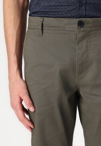 Olivgrüne Hose aus strukturiertem Stoff, mit Knopfverschluss, klassischen Taschen und geradem Bein.