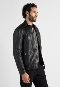 Svart läderjacka med ståkrage, quiltade axeldetaljer och två dragkedjefickor på framsidan. Randig skjorta under.