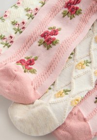 Dwie pary dzianinowych skarpet z kwiatową haftem, jedna różowa z czerwonymi kwiatami, druga kremowa z żółtymi kwiatami.