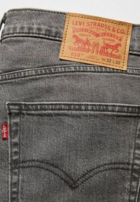 Mörkgrå denimjeans med slim fit och rak benform, med en tan läderlapp märkt "Levi Strauss & Co." på bakhöften.