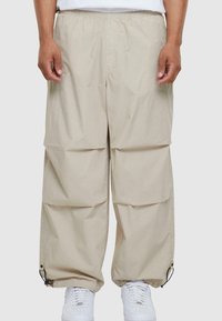 Beige cargo bukser med løst fit, elastisk talje og sidelommer. Har justerbare manchetter med snore, lavet af letvægtsstof.