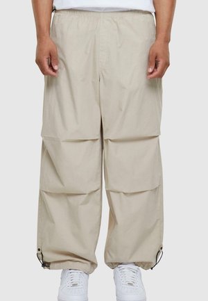 Pantalons cargo beiges avec une coupe ample, taille élastique et poches latérales. Présente des poignets ajustables avec des cordons de serrage, fabriqués en tissu léger.
