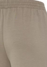 Gros plan sur la ceinture élastique beige et la texture du tissu d'un pantalon ou short décontracté.