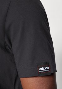 Svart t-skjorte med korte ermer og en glatt tekstur. Har et sydd Adidas-merke med "Copa Mundial" i hvite og røde detaljer på ermet.