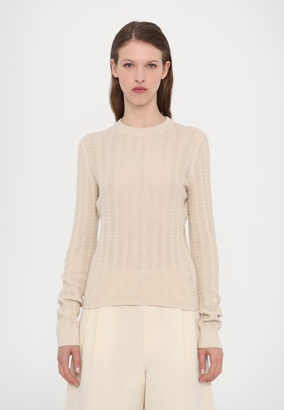 Beige knitted sweater with a textured pattern, featuring a crew neckline and long sleeves, paired with light-colored wide-leg trousers.