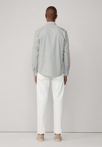 Camicia a righe con maniche lunghe e colletto, abbinata a pantaloni bianchi e scarpe beige. Tessuto liscio, design aderente e polsini arrotolati.