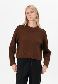 Barna, cropped pulóver bordázott textúrával és kerek nyakkivágással, hosszú ujjakkal és lazán illeszkedő fazonnal, fekete nadrággal párosítva.